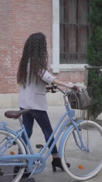 Kiharatukkainen nainen polkupyörällä kävelee kaupungin puiston sivuraiteella. Jäljityslaukaus - Pystysuora - Materiaali, video