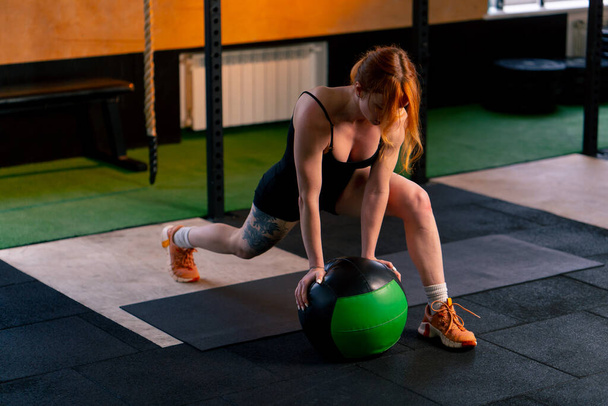 ve sportovním klubu rusovlasá trenérka dělá rozcvičku pro její nohy opírající se o míč - Fotografie, Obrázek
