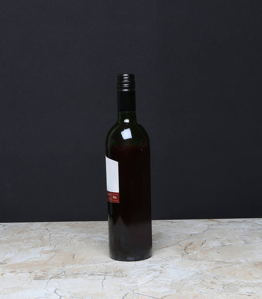 Veredeln Sie Ihr Weinerlebnis mit unserer exquisiten Rotweinflasche vor auffallend schwarzem Hintergrund, die ihre Eleganz und Raffinesse mit einem Hauch von Luxus unterstreicht. - Foto, Bild