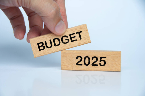 Beyaz arka planda Budget 2025 yazısıyla el ele tutuşan ahşap blok. Yıllık bütçe kavramı - Fotoğraf, Görsel