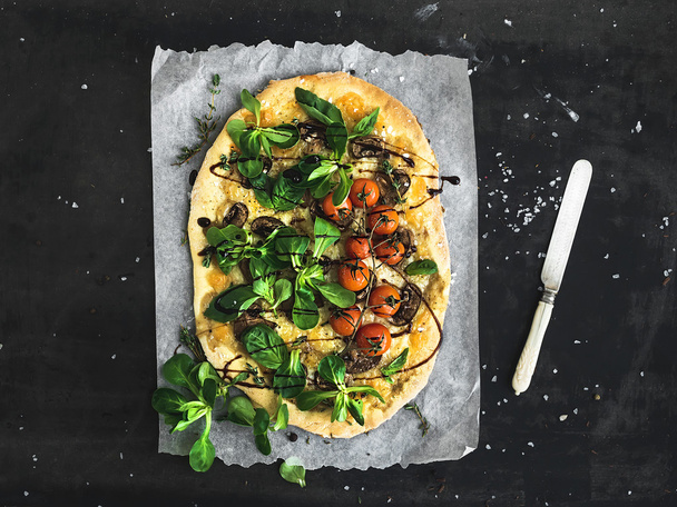 Rustic homemade pizza with fresh lambs lettuce, mushrooms and cherry-tomatoes over dark grunge background - Photo, Image