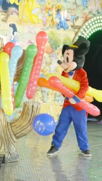 Valencia kermis - Man in Mickey Mouse kostuum geeft weg opgeblazen ballonnen wanneer kinderen rijden trein achtbaan 's nachts - FullHD Verticale video - Video