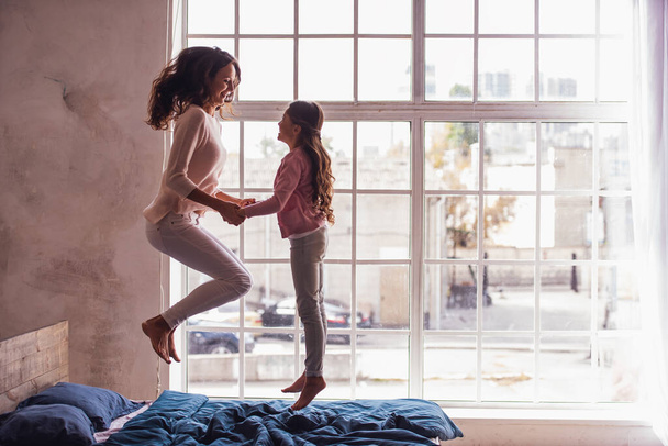 Mooie moeder en dochter zijn het hebben van pret terwijl het springen op bed thuis - Foto, afbeelding