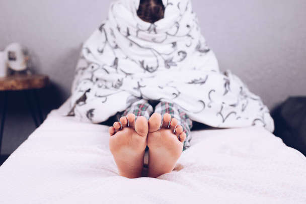Nackte Füße. Der Junge liegt mit einer Decke bedeckt im Bett. Fuß und Ferse. Plattfuß - Foto, Bild
