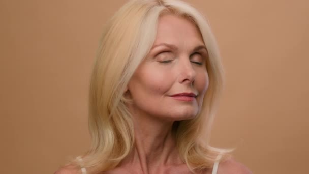 Közelkép gyönyörű kaukázusi idős nő mosolygós középkorú 50-es évek idős hölgy modell boldog mosoly bézs stúdió háttér szépség arc ráncok bőrápolás anti-aging emelő eljárás plasztikai sebészet - Felvétel, videó
