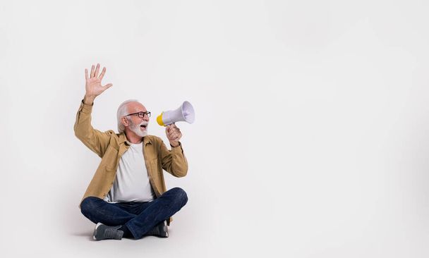 Старший бизнесмен с поднятой рукой крича над мегафоном и глядя в сторону на белом фоне - Фото, изображение