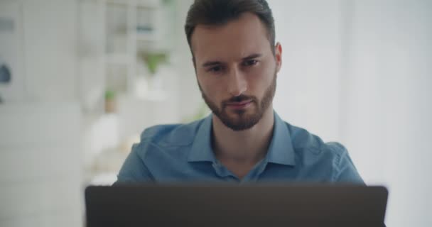 Lockdown disparo de confianza joven barbudo hombre de negocios utilizando el ordenador portátil mientras está sentado en el espacio de trabajo corporativo - Imágenes, Vídeo