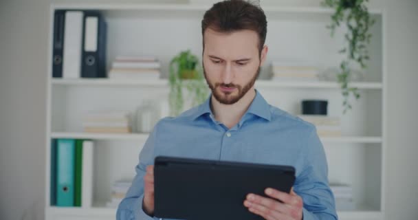 Zelfverzekerde knappe jonge zakenman schrijven strategie op digitale tablet met stylus terwijl staan op corporate werkruimte - Video