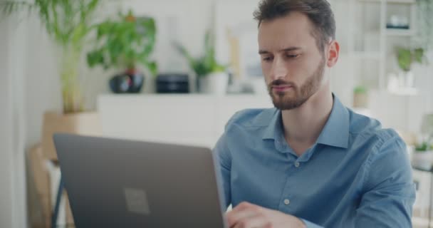 Уверенный молодой мужчина профессионально просматривает интернет на ноутбуке в корпоративном рабочем пространстве - Кадры, видео