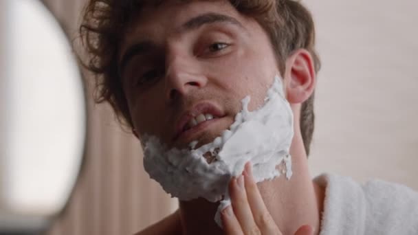 Közelkép portré fejlövés kaukázusi szakállas borotválatlan sörte férfi férfi kenet hab az arcon és állkenet borotválkozás hab gél borotválkozás előkészítéséhez arc bőrápolás higiéniai eljárás kozmetikai szépség - Felvétel, videó