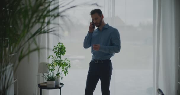 Důvěryhodný mladý muž podnikatel diskutovat o strategii na výzvu přes smartphone, zatímco stojí proti oknu na pracovišti - Záběry, video