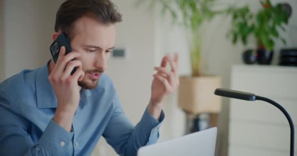 Jóképű fiatal üzletember beszél stratégia hívás okostelefonon keresztül, miközben ül a laptop vállalati irodában - Felvétel, videó
