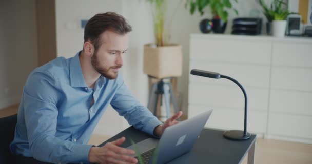 Giovane imprenditore di sesso maschile fiducioso che spiega la strategia sulla videochiamata tramite laptop mentre lavora nello spazio di lavoro aziendale - Filmati, video