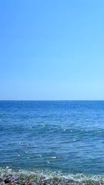 Vista di piccole onde di mare blu, cielo azzurro senza nuvole e linea di orizzonte in una giornata calda estiva soleggiata. increspature su acqua e bagliore di sole bianco su superficie d'acqua. Mare calmo. Tempo calmo senza vento. Verticale - Filmati, video