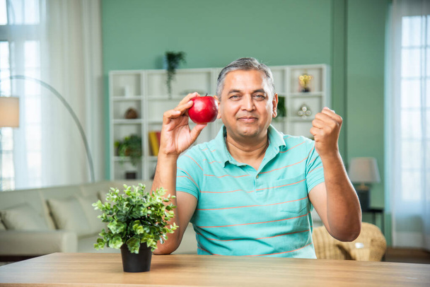 indian senior man eating or presenting an apple - Photo, Image
