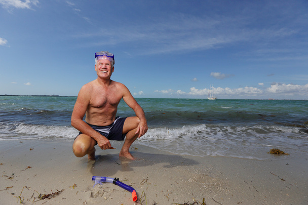 Homme âgé accroupi au bord de la plage
 - Photo, image