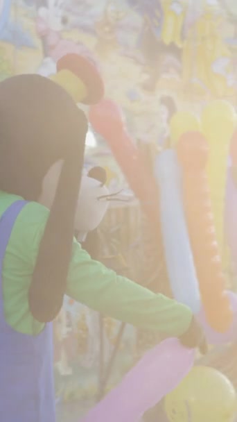 Goofy a Mickey Mouse Disney postavy povzbudit lidi na koni kidsl vlak horská dráha s balónky ve Valencii veletrhu - FullHD Vertikální video - Záběry, video