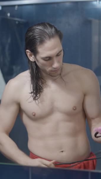 Joven hombre metrosexual saca de un cajón un secador de pelo pin y se seca el pelo delante de un espejo - MIddle shot - Vídeo vertical - Metraje, vídeo