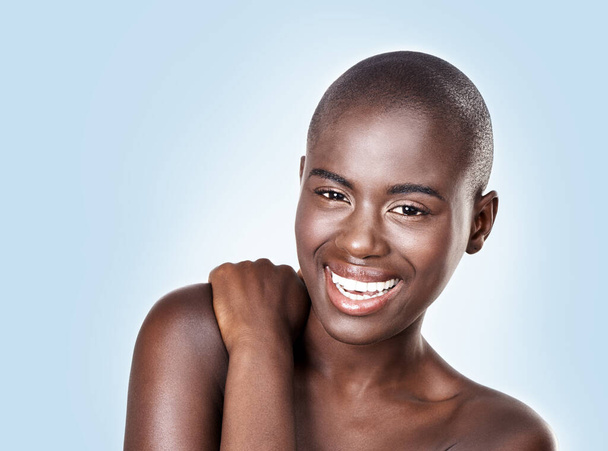 Portrait, beauty and smile with bald black woman in studio on blue background for natural wellness. Face, skincare and aesthetic with happy young model at spa for cosmetics, facial or dermatology. - Photo, Image