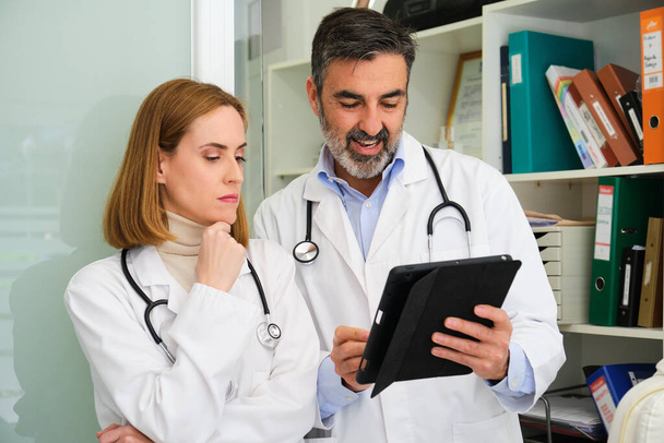 Dva profesionální lékaři diskutující o lékařských zprávách a pomocí tabletu v kanceláři. - Fotografie, Obrázek