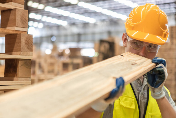Man wearing safety uniform and yellow hard hat working checking quality wooden products at workshop manufacturing wooden. Male carpenter worker wood warehouse industry. - Photo, Image