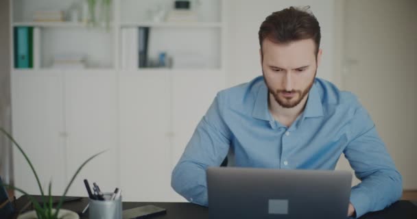 Замкнений знімок зосередженого молодого гарного бізнесмена, який використовує ноутбук, сидячи за столом, працюючи в офісі - Кадри, відео