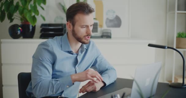 Zelfverzekerde jonge mannelijke professional legt strategie op video oproep via laptop tijdens het werken op corporate werkruimte - Video