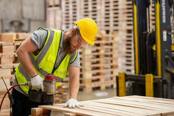 Gépész ács visel biztonsági egyenruhát és sárga kemény kalap dolgozik elektromos körömágyú a fa műhely gyártás. Férfi munkás faipari raktár ipar. - Fotó, kép