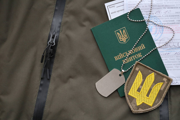 Военный жетон или армейский билет с уведомлением о мобилизации лежит на зеленой украинской военной форме в закрытом помещении - Фото, изображение