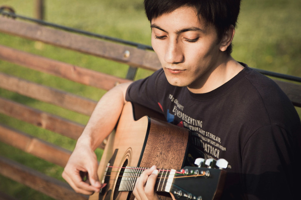young boy playing a guitar on a bench - 写真・画像