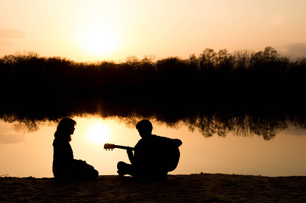silhouette of a young boy and girl on the beach with a guitar - Фото, изображение