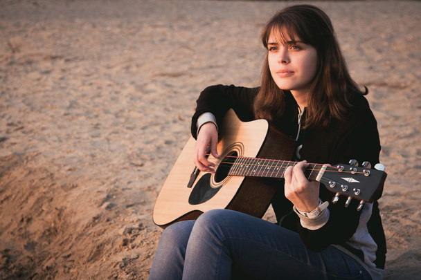 young girl playing guitar sitting on the sand - Fotó, kép