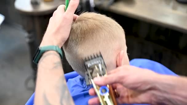 Rückenansicht des Friseurs, der Jungen den Kopf rasiert. Kompetenter Friseur mit Elektrorasierer beim Friseur. Kleiner Kunde bekommt stylische Herrenfrisur. - Filmmaterial, Video