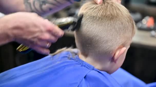 Вид сзади на голову парикмахера, бреющего мальчиков. Компетентный парикмахер с использованием электробритвы. Маленький клиент делает стильную мужскую стрижку. - Кадры, видео