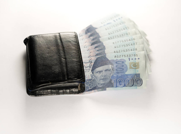 Tysiąc tysięcy rupii banknotów wyrównanych z czarnym skórzanym portfelem. Pakistan State Bank oficjalne banknoty walutowe 2024 izolowane na białym tle. - Zdjęcie, obraz