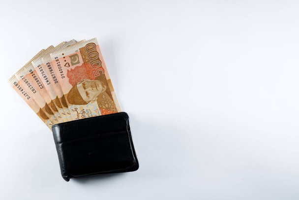 Pięć tysięcy banknotów 5000 rupii wyrównanych z czarnym skórzanym portfelem. Pakistan State Bank oficjalne banknoty walutowe 2024 izolowane na białym tle. - Zdjęcie, obraz