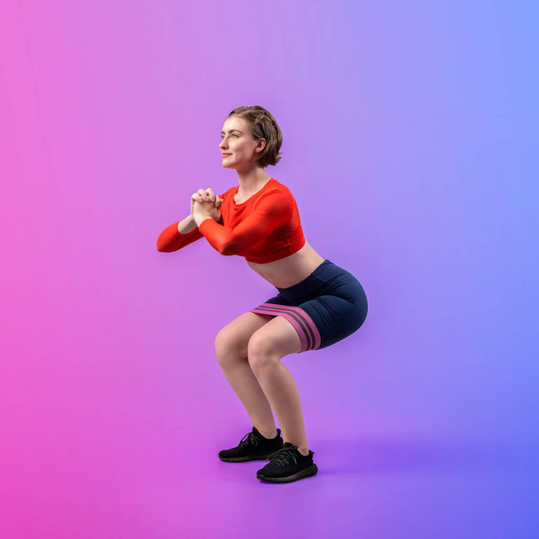 Teljes testhosszú vidám lövés sportos és sportos fiatal nő fitness rugalmas ellenállás sáv guggoló testmozgás testtartás elszigetelt háttérrel. Egészséges aktív és testápoló életmód. - Fotó, kép