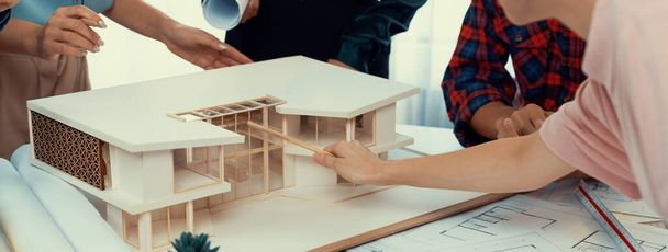 Architect team analyse en brainstormen over woningbouw aan vergadertafel met huismodel, blauwdruk en architectonische apparatuur verspreid rond. Creatief ontwerp en teamwork. Ontluikende. - Foto, afbeelding