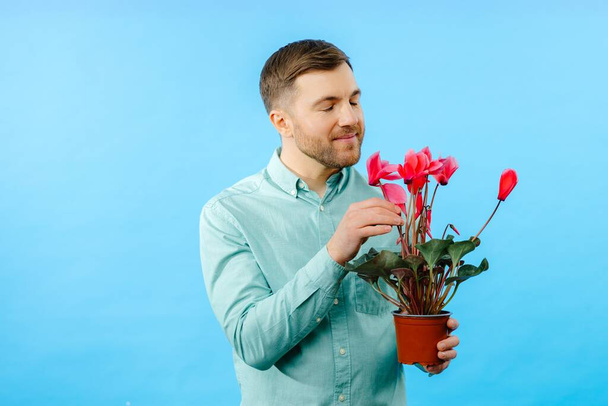 Мужчина держит в руках горшок с красными цветами. Весенние цветы ко Дню матери, Международному женскому дню, дню рождения. - Фото, изображение