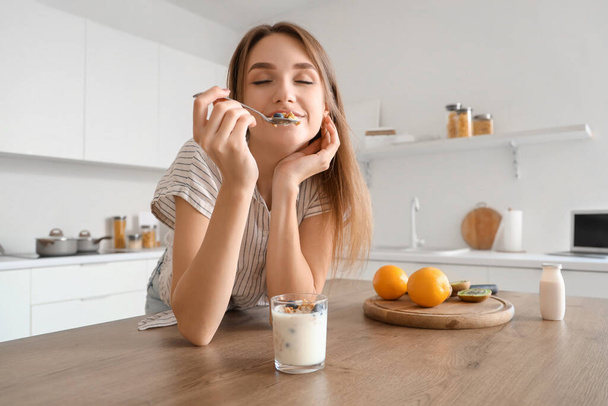 Young woman eating tasty yoghurt in kitchen - Photo, Image
