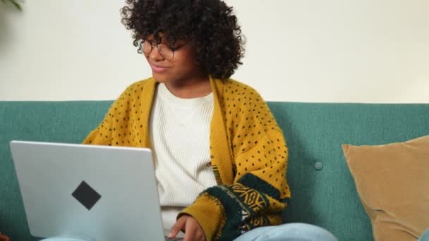Egy afro-amerikai lány laptopot használ az otthoni irodájában, és a képernyőt nézi, amint chatel, miközben e-maileket ír. Fiatal nő, hogy virtuális találkozó online chat video call konferencia. Otthoni tanulás - Felvétel, videó