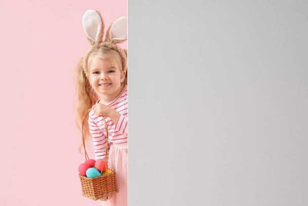Linda niña con orejas de conejo, huevos de Pascua y póster en blanco sobre fondo rosa - Foto, Imagen