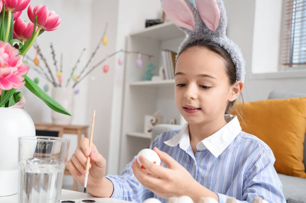 Cute little girl with bunny ears painting Easter eggs in living room - Photo, Image