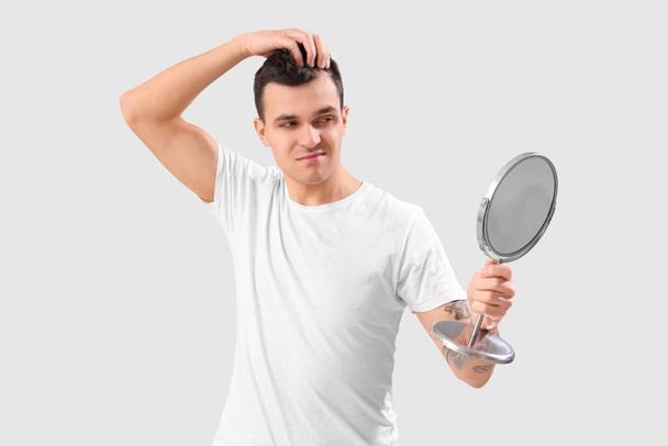 Jeune homme bouleversé avec problème de perte de cheveux regardant dans le miroir sur fond clair, gros plan - Photo, image