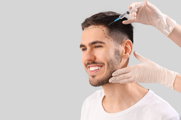 Jeune homme au front marqué recevant une injection pour la croissance des cheveux sur fond clair, gros plan - Photo, image