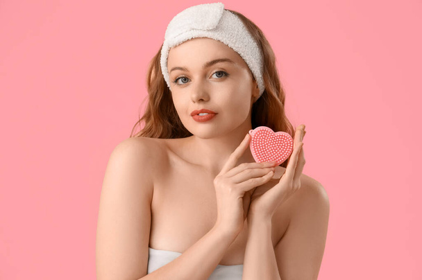 Όμορφη νεαρή γυναίκα στο μπάνιο κεφαλόδεσμο με σφουγγάρι σε σχήμα καρδιάς σε ροζ φόντο, closeup - Φωτογραφία, εικόνα