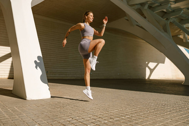 Spor kıyafetli genç bir kadın arka planda duvarla havaya sıçrıyor. Yüksek kalite fotoğraf - Fotoğraf, Görsel