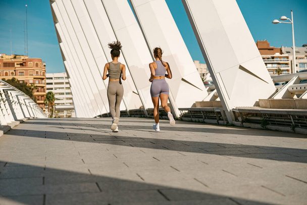 Dvě mladé ženy ve sportovním oblečení běhají po moderních budovách. Koncept aktivního životního stylu - Fotografie, Obrázek