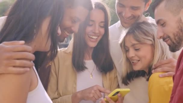 Young group of gen z people having fun using cell phone together outside watching social media. Cheerful community of student enjoying content on smartphone app. Young multiethnic group of friends  - Footage, Video