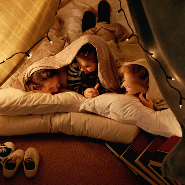 Crianças, felizes e dormindo na tenda à noite com conversa, vínculo e aventura de férias ou férias. Jovens amigos ou crianças por luzes de fadas, travesseiros e cobertor em casa para contar histórias divertidas. - Foto, Imagem